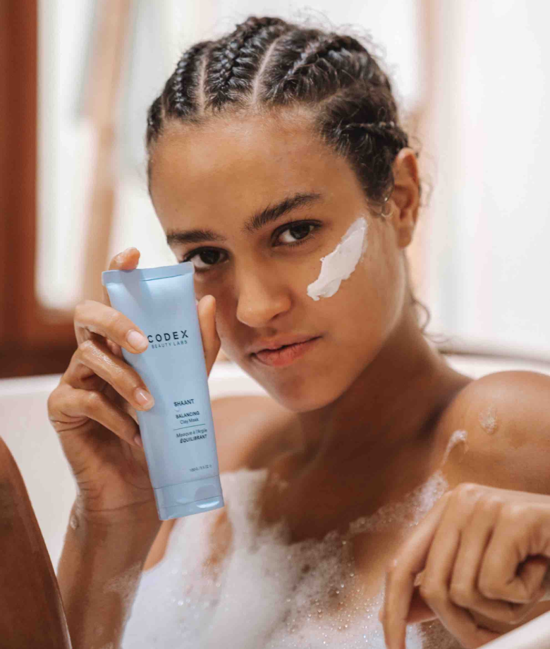 Woman holding a bottle of Shaant in a bathtub. 